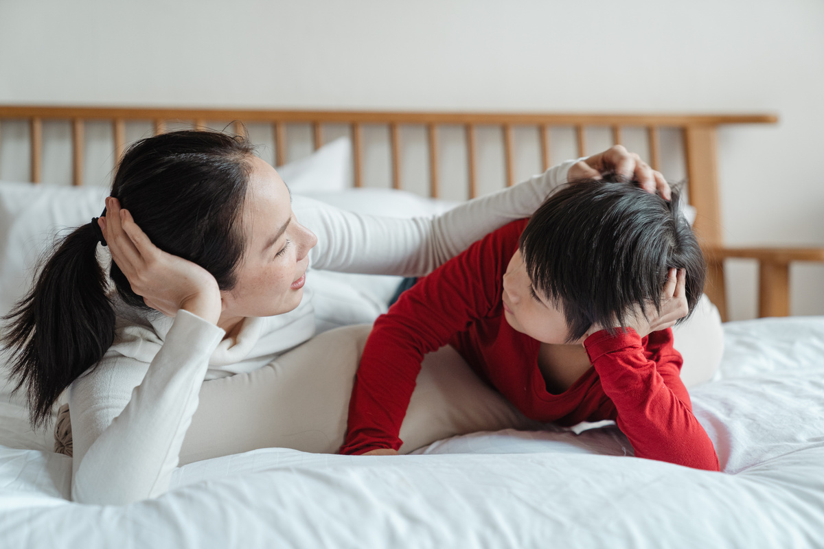 Caring mother patting little son on head on bed